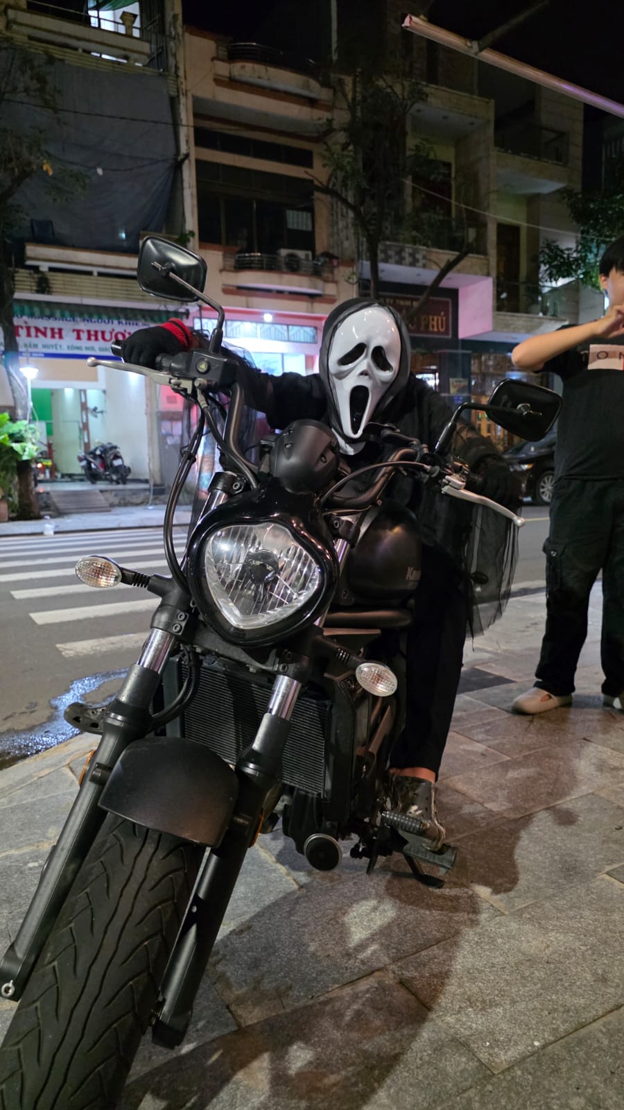 Guest wearing a Ghostface costume posing on a motorbike